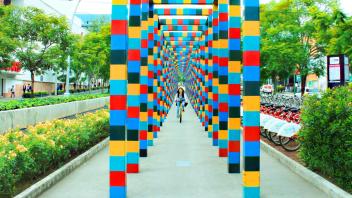Image of a student riding a bike between a row of colorful pillars