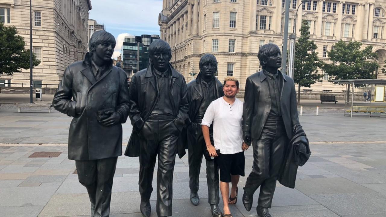 The 5th Beatle: Gonzales stands among four statues commemorating the members of The Beatles on a London street. (Courtesy of Adrian Gonzales) Gonzales stands among four metal statues of The Beatles on a London street.