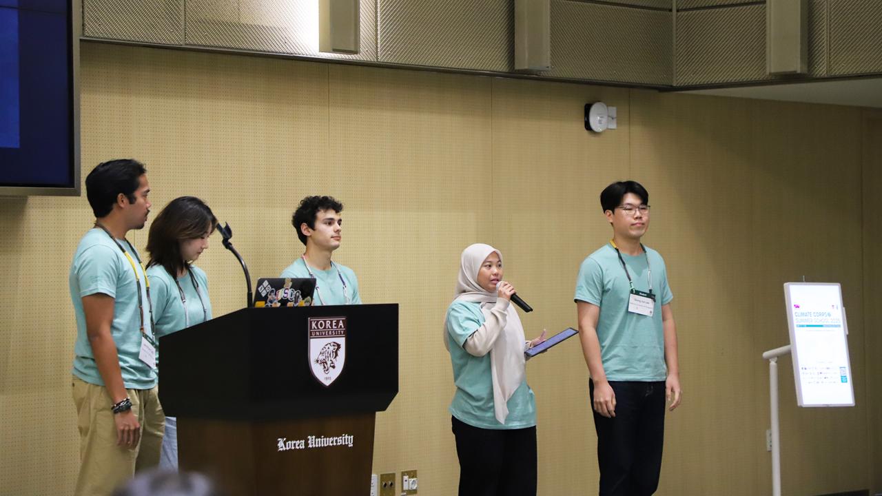 A group of five individuals in matching teal shirts presents at a podium.