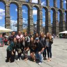 Group of students posing in front of a historic stone aqueduct in Spain under a blue sky.