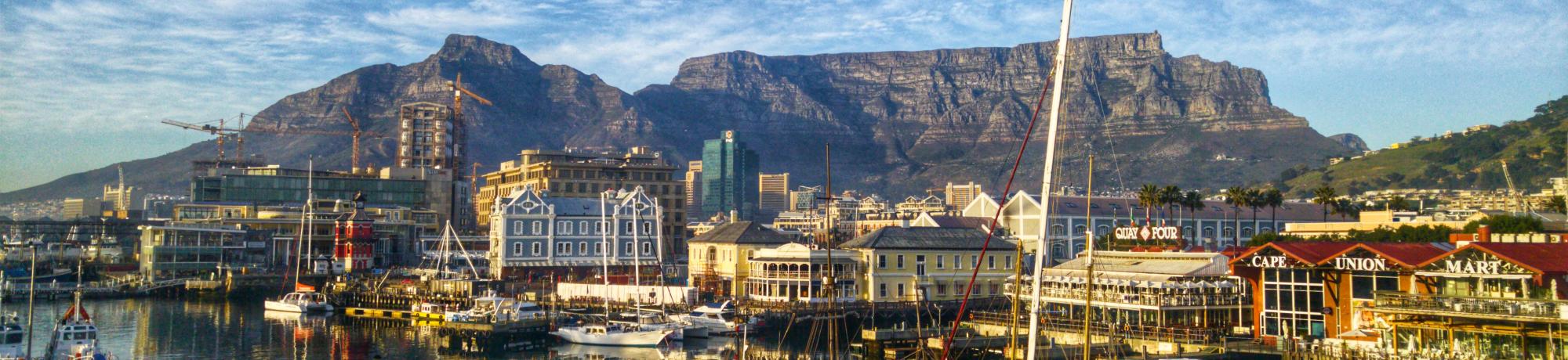 Waterfront with boats and colorful buildings, set against a large, flat-topped mountain range.