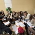 Small group seated in a circle reviewing papers in a beige meeting room, photo