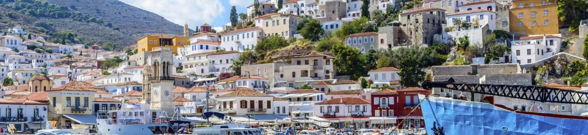 Colorful coastal village with boats in the foreground and hills in the background under blue sky.