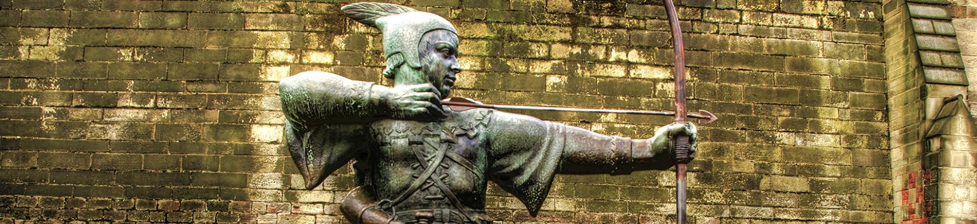 Bronze statue of Robin Hood in Nottingham, aiming a bow, set against a stone wall.