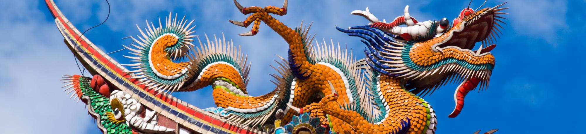 Colorful dragon sculpture atop a traditional building against a blue sky.